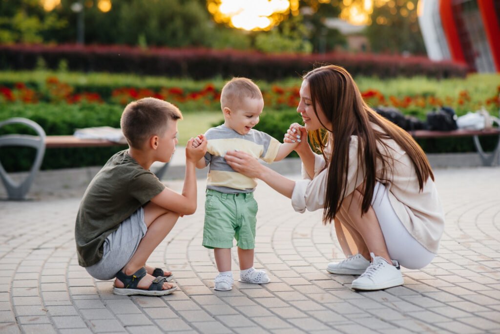 A baby interacting with mom and brother in the park. 